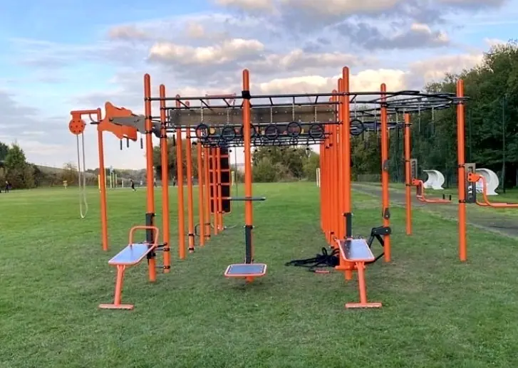 Équipements de fitness extérieurs orange et noir dans un parc verdoyant.