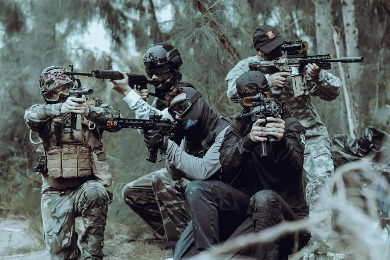 Quatre joueurs d'airsoft en tenue tactique visent dans les bois.