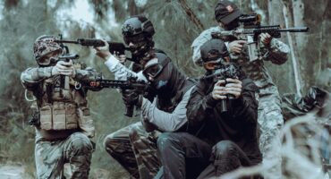Quatre joueurs d'airsoft en tenue tactique visent dans les bois.