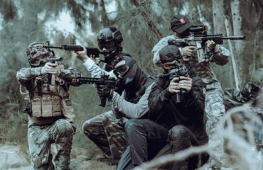 Est-ce que l’airsoft est un sport ? Analyse complète en 2026 Quatre joueurs d'airsoft en tenue tactique visent dans les bois.