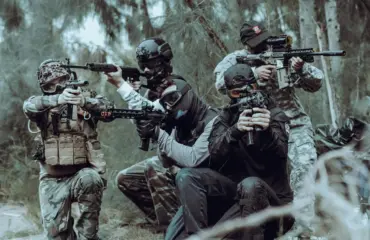Est-ce que l’airsoft est un sport ? Analyse complète en 2026 Quatre joueurs d'airsoft en tenue tactique visent dans les bois.