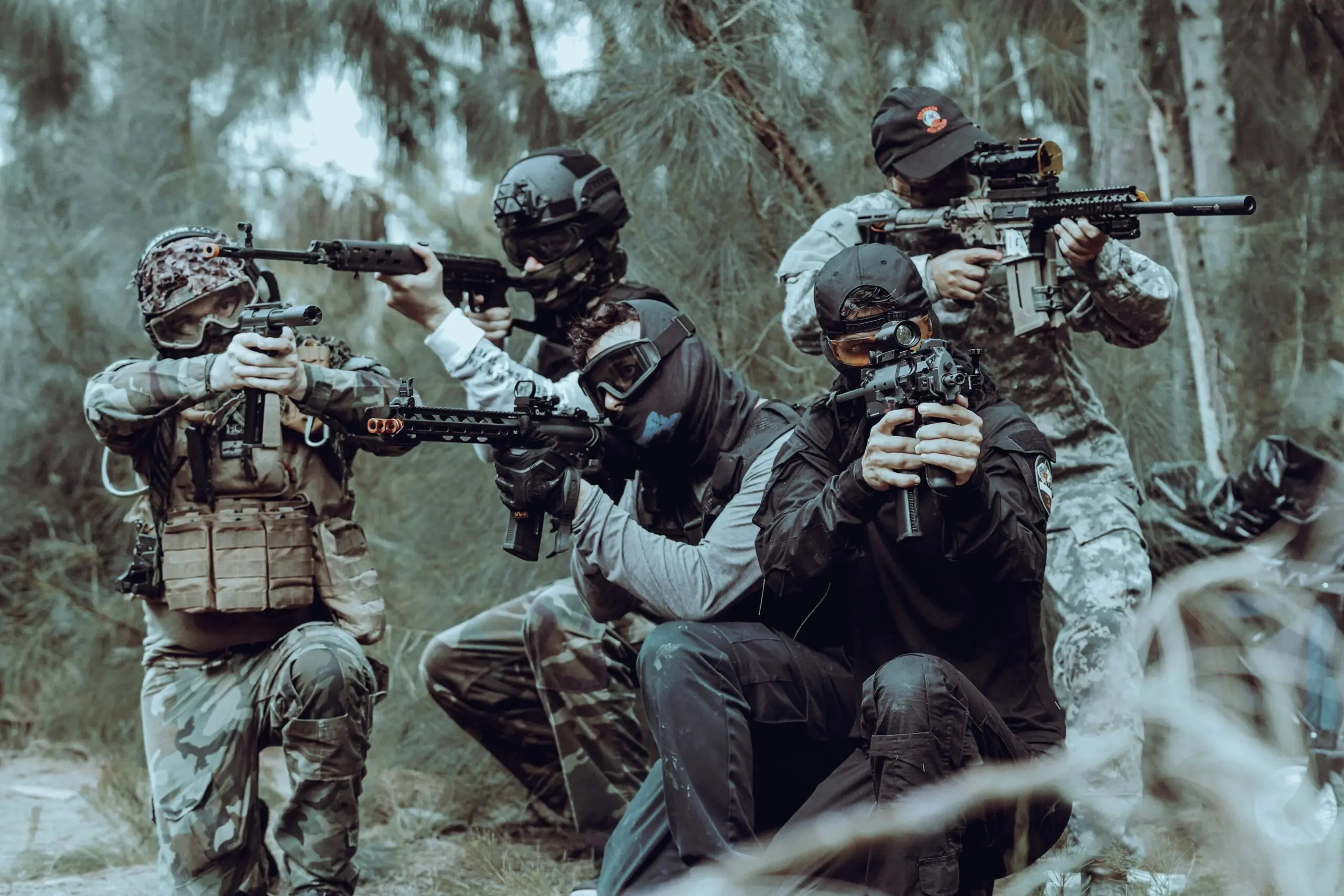 Quatre joueurs d'airsoft en tenue tactique visent dans les bois.