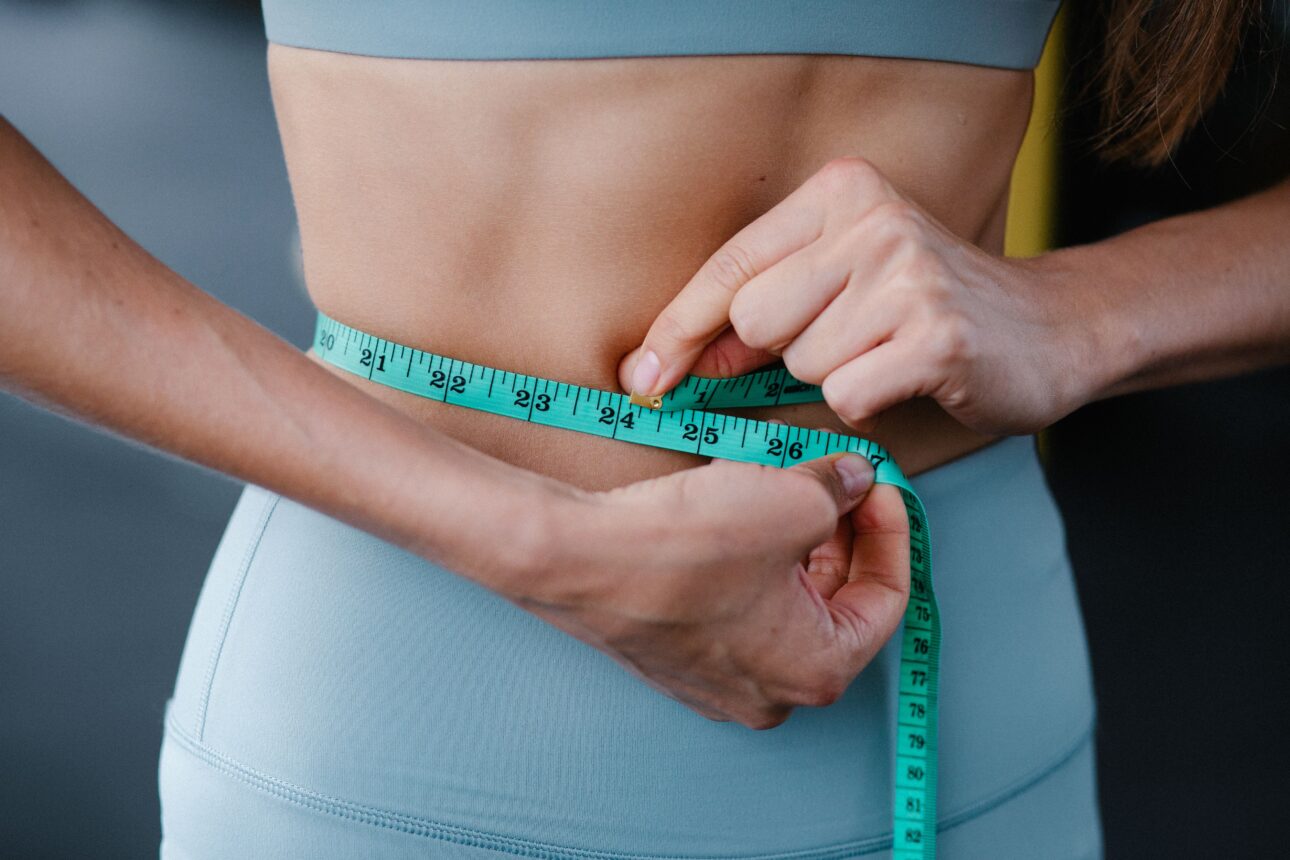 Femme mesurant son tour de taille avec un mètre ruban vert.