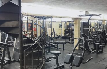 salle de sport et bruit de voisinage comment traiter les plaintes par le sol Gym élégante avec escalier en colimaçon et machines de musculation modernes.