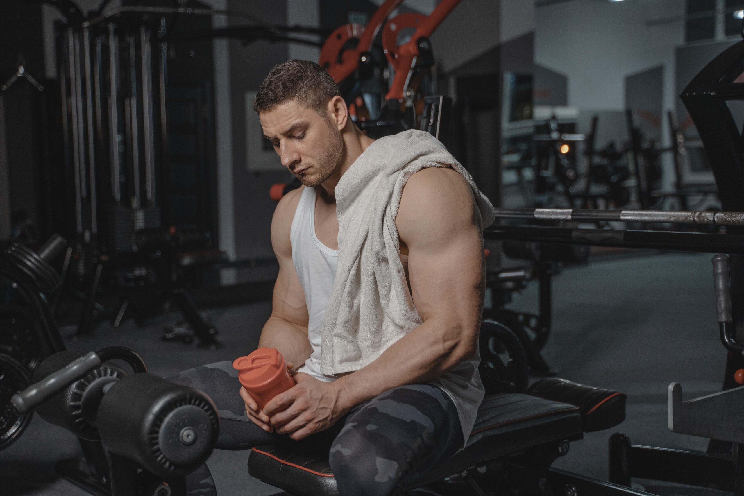 Homme musclé au repos en salle de sport, tenant un shaker.